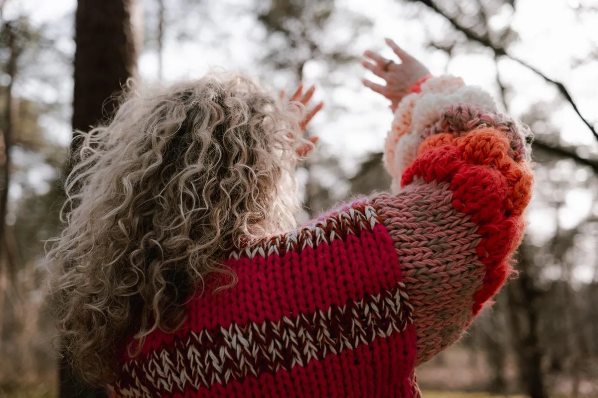 Een vrouw in een rode trui steekt haar armen in de lucht
